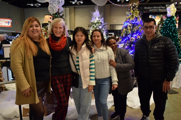 6 people standing by decorated trees at Festival of Trees