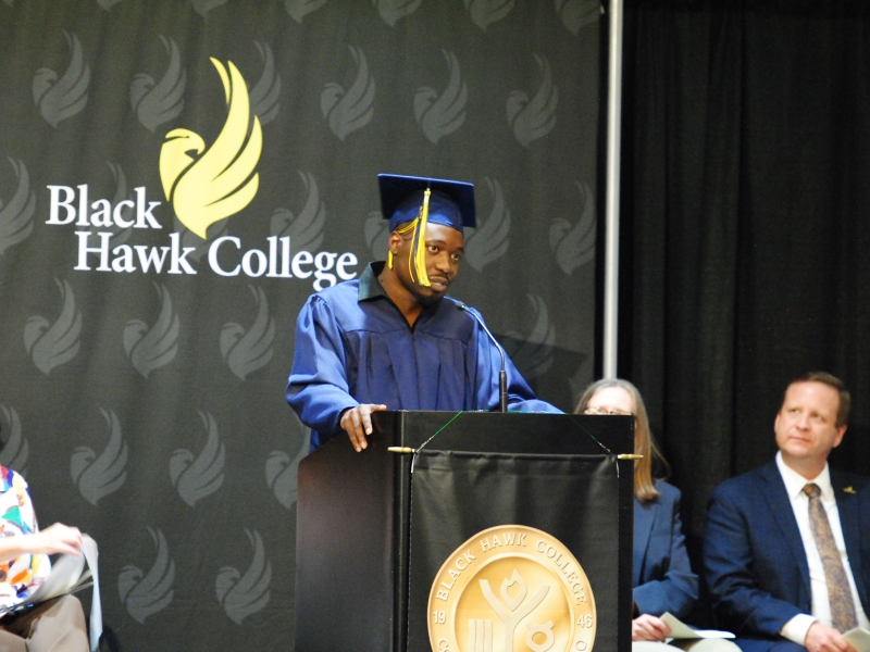 GED grad wearing cap & gown and speaking at podium on stage