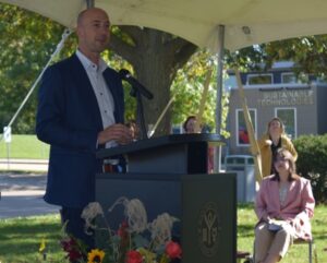 Paul Rumler speaking at podium outdoors under tent