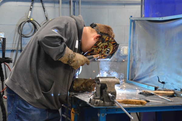 high school student wearing protective equipment and welding