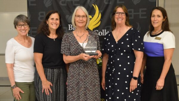 5 people standing in front of backdrop with 1 holding an award