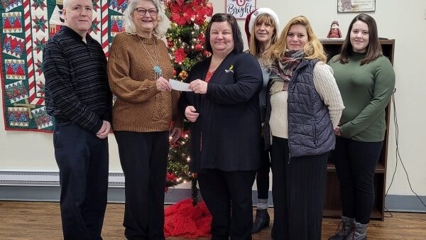 6 people with check donation standing in front of Christmas tree