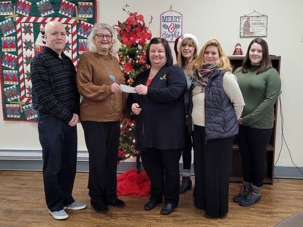 6 people with check donation standing in front of Christmas tree