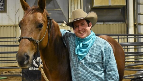 male student wearing cowboy hat with his arm draped across his horse