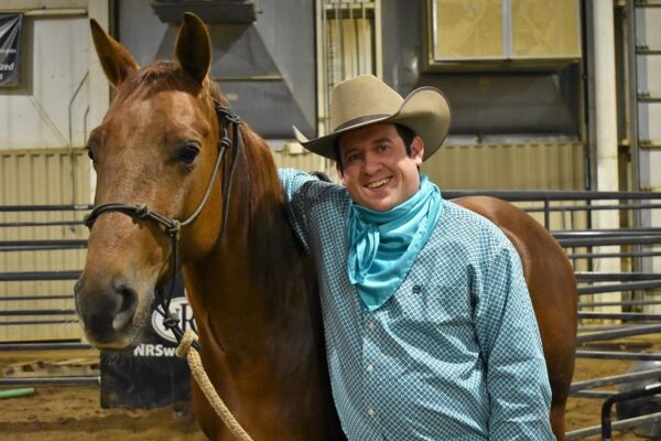 male student wearing cowboy hat with his arm draped across his horse