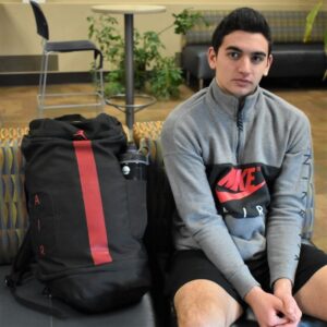 male student sitting on couch with backpack next to him