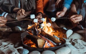 hands holding sticks to roast marshmallows over outdoor fire