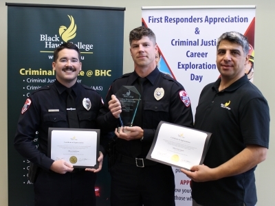 3 people with certificates & awards in front of banners