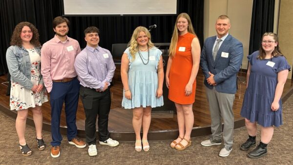 7 students standing by stage in auditorium at East Campus