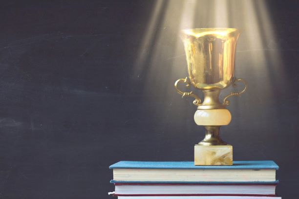 golden trophy on pile of books in front of blackboard