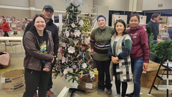 5 people standing with decorated tree at Festival of Trees setup day