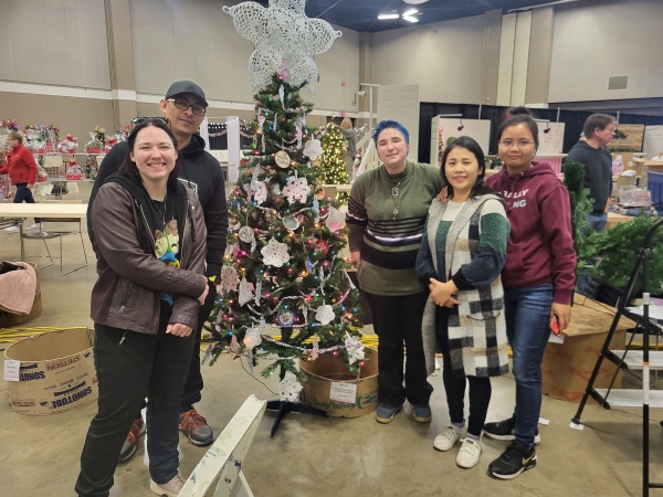 5 people standing with decorated tree at Festival of Trees setup day