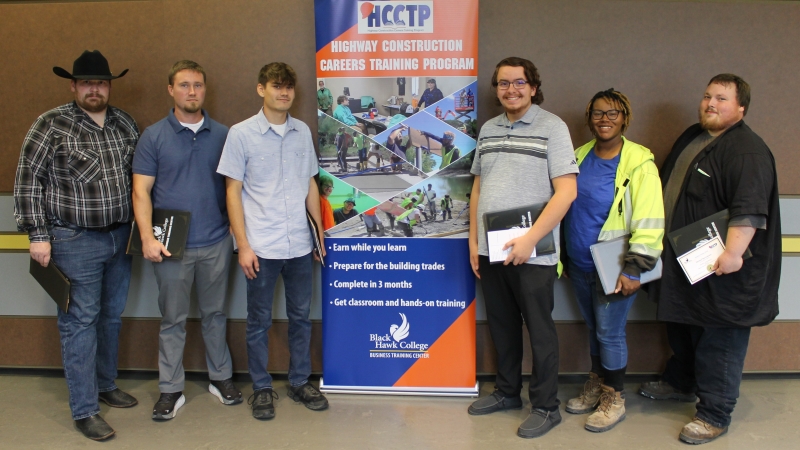 6 people standing by banner and smiling at camera