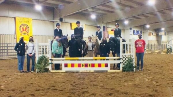 6 students standing in dirt next to 4 people sitting on horses