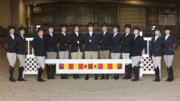 13 hunt seat riders standing in arena with banner