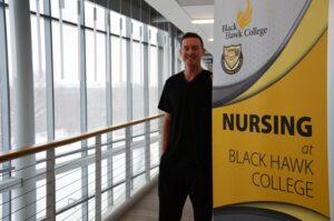 Ian Hutto standing next to yellow BHC nursing sign, next to windows