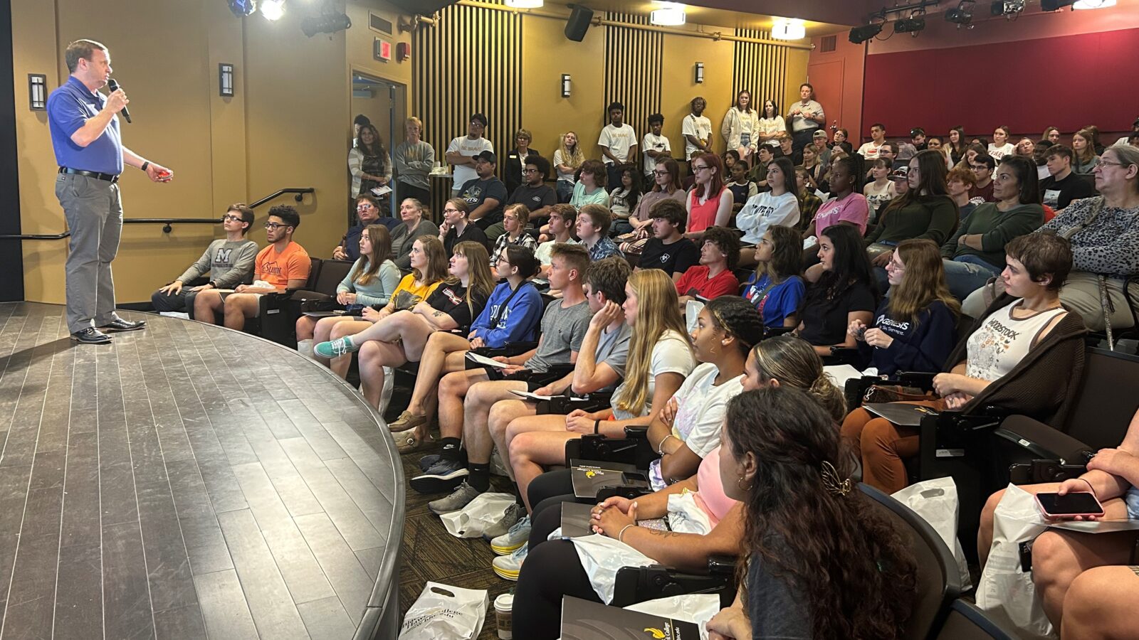 Students in a large lecture hall listen intently to a speaker on the stage.