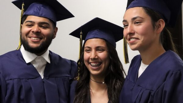 3 smiling grads in caps and gowns