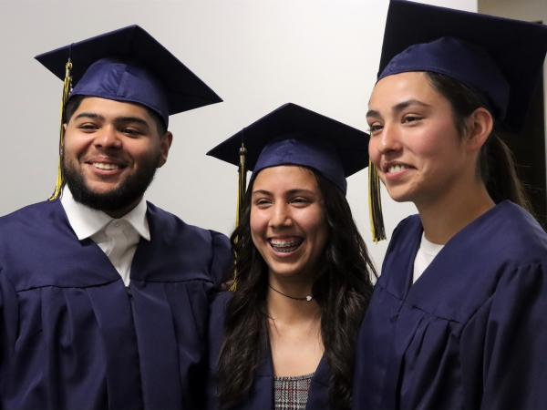 3 smiling grads in caps and gowns