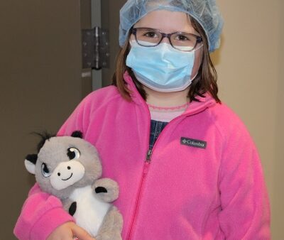 child wearing surgical mask and cap and holding stuffed animal