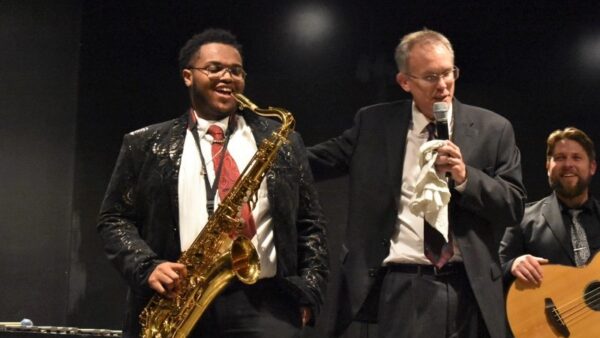 student with saxophone laughs while professor tells a story during a concert