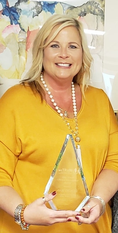 smiling woman in yellow shirt holding triangular acrylic award