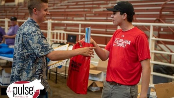 BHC grad hands off a bag to another person in an indoor arena