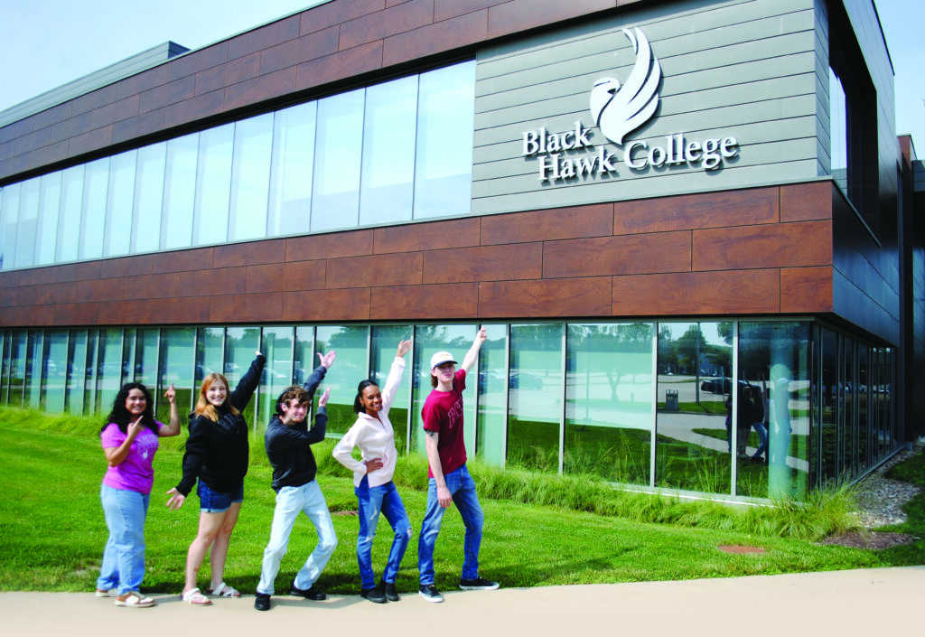 Five students pointing to a new Black Hawk College academic building.