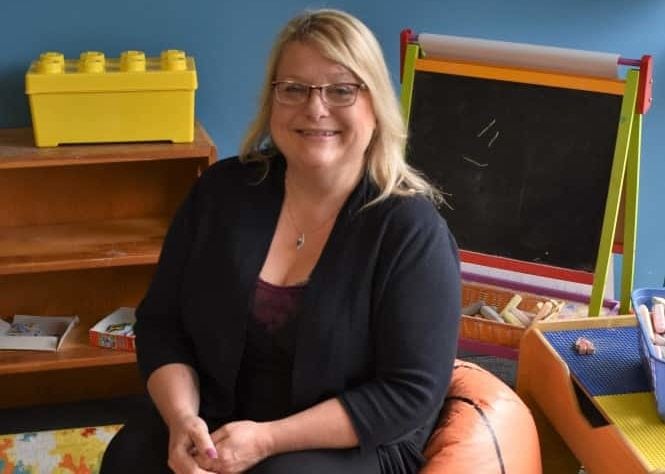 BHC graduate Kristie Amato sitting on basketball beany bag chair with child chalk board behind her