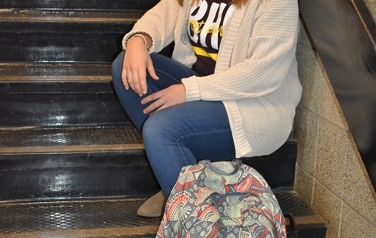 female student sitting on stairs with book bag in front of her