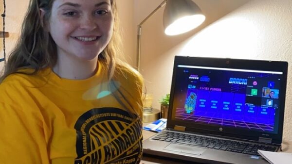 smiling student sitting at a desk while attending a virtual conference for Phi Theta Kappa