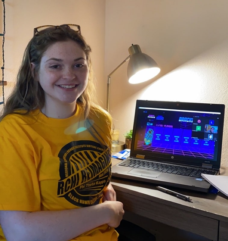 smiling student sitting at a desk while attending a virtual conference for Phi Theta Kappa