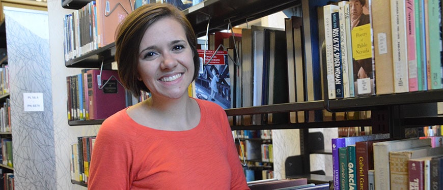 Woman in orange shirt standing in front of library book shelves