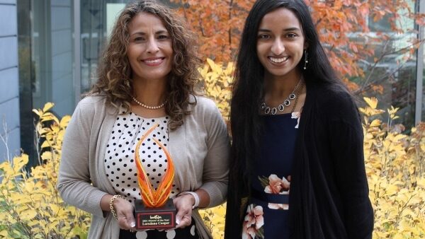 Loredana Cooper holding award with Saheli Sheth standing outdoors on fall day