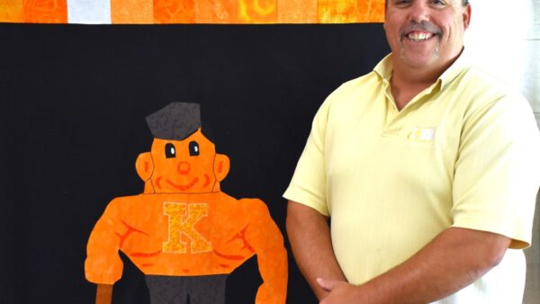 Kewanee High School teacher standing in front of a quilt featuring the school's mascot, a boilermaker