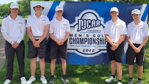 5 golfers standing outdoors in front of tournament sign