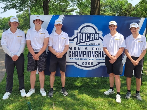 5 golfers standing outdoors in front of tournament sign