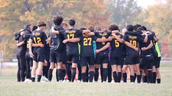 soccer players huddling on field with arms around each other