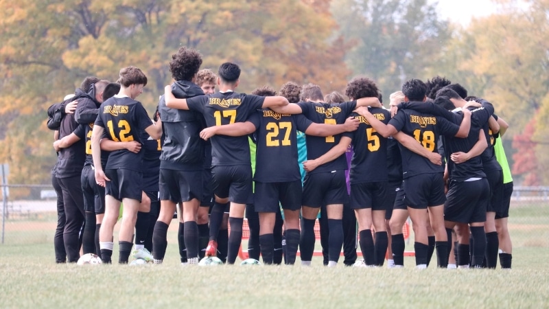 soccer players huddling on field with arms around each other