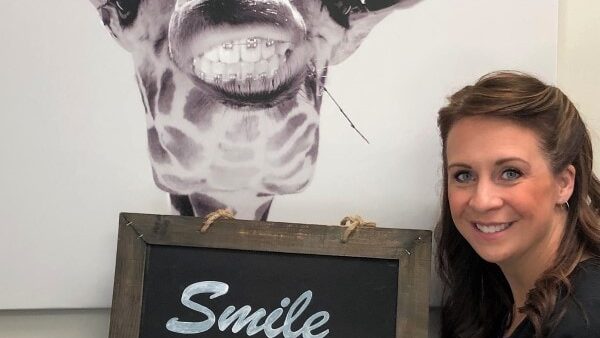 woman holding a sign that reads smile loud with an image of a giraffe wearing braces behind her