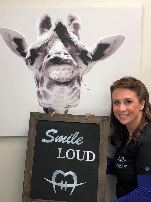 woman holding a Smile LOUD sign with art of a giraffe wearing braces behind her