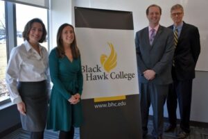 4 people standing in front of Black Hawk College banner