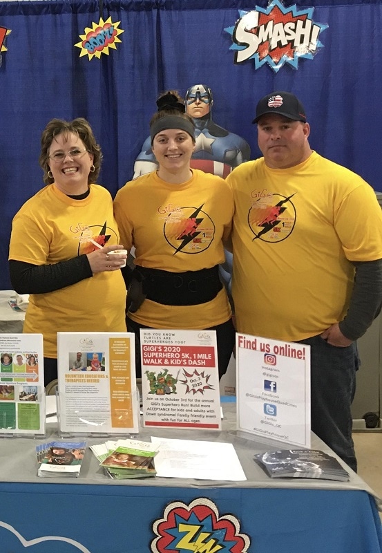 woman stands behind an informational table with her daughter and husband