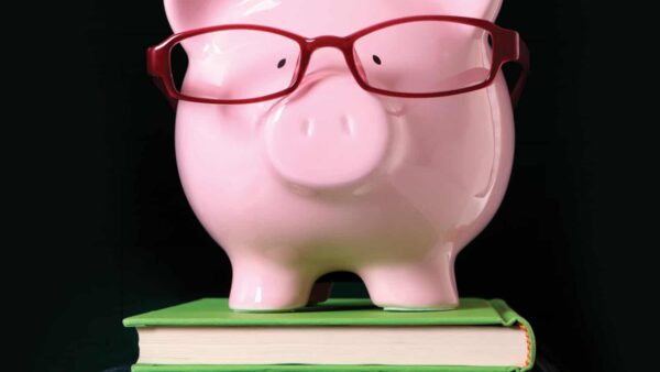 pink piggy bank wearing red glasses on stack of books