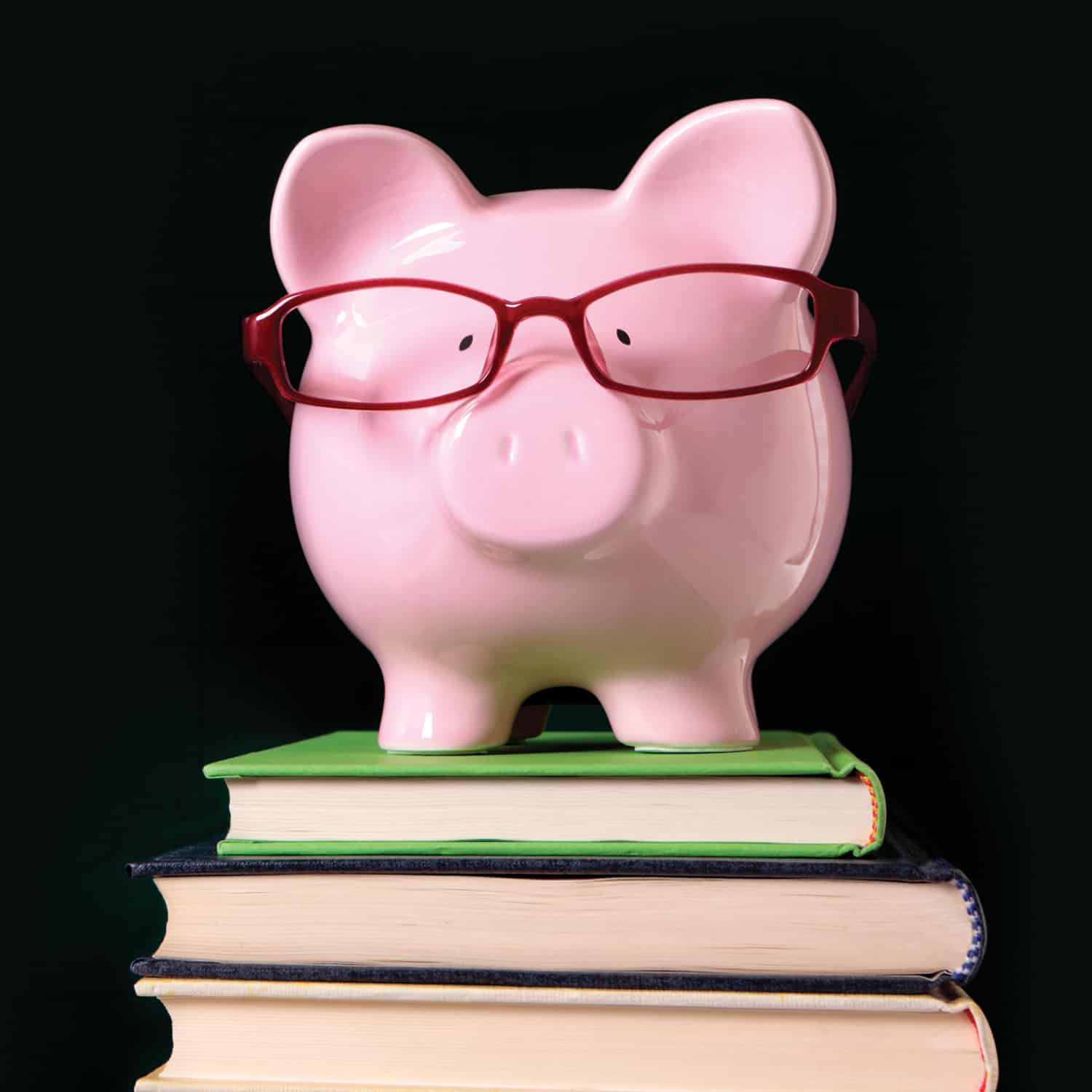 pink piggy bank wearing red glasses on stack of books