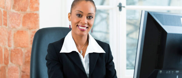 Business woman in a suit sits in front of a computer in an office setting.