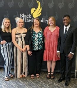 5 people standing in front of backdrop with college logo