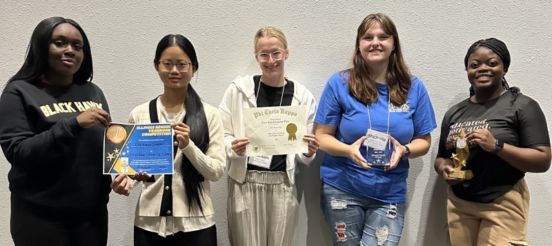 5 smiling students standing together holding awards and certificates