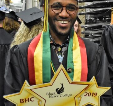 Graduate wearing black cap and gown holding BHC 2019 sign