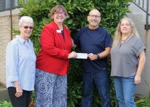 4 people standing outdoors with a check